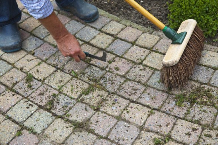 man brushing grass off stone pathway for fall maintenance