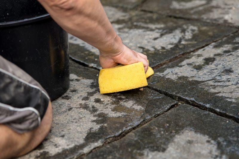 man scrubbing stone walkway with sponge